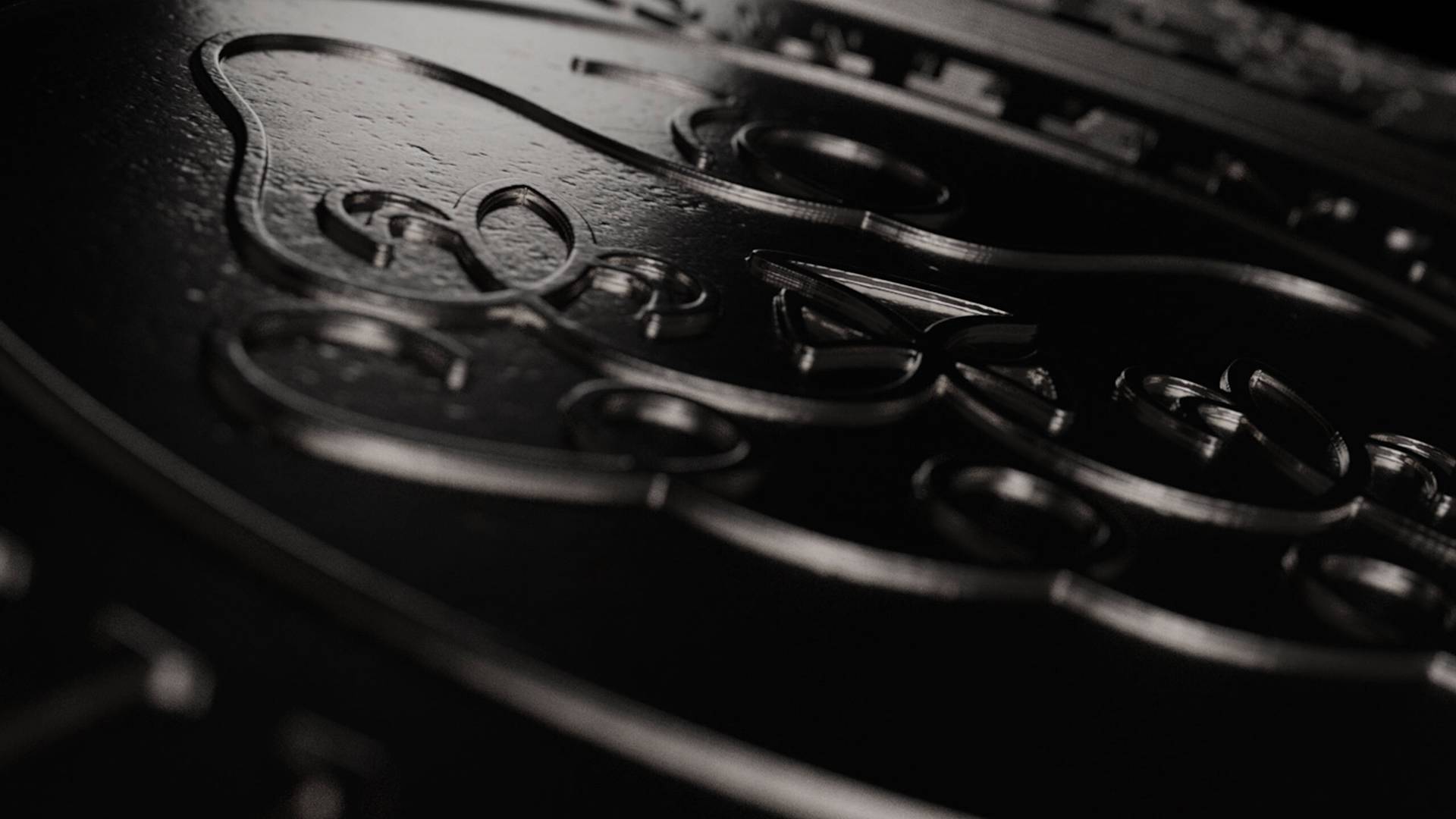 Close-up of a dark, embossed metallic surface with intricate, swirling patterns and textures highlighted by soft light and shadows.