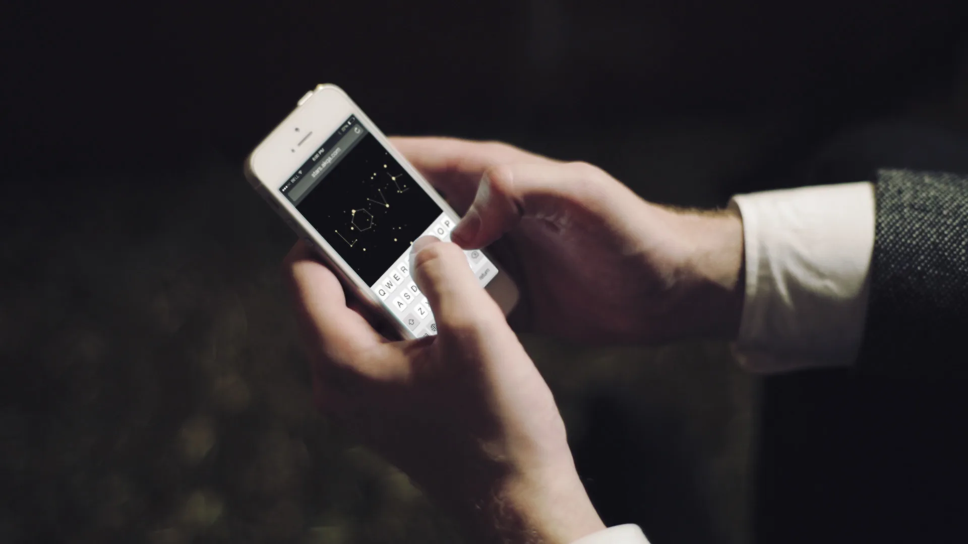 A person holding a smartphone and typing a message. The screen displays the word LOVE written in a stylized font on a black background. The person is wearing a white shirt and a grey jacket.