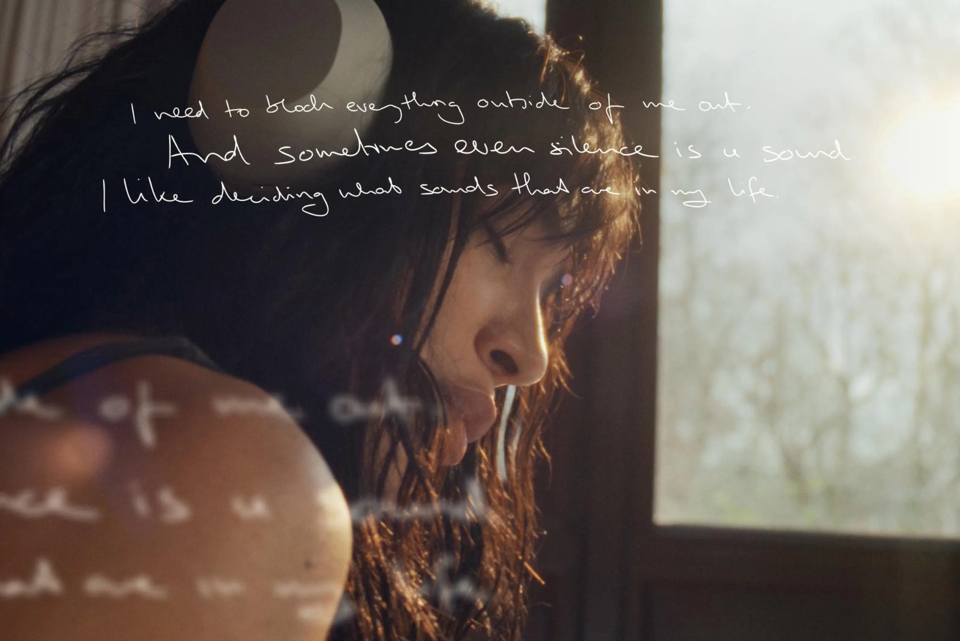 A woman wearing headphones looks down pensively near a sunlit window. Handwritten text overlays the image, reading: I need to block everything outside of me out. And sometimes even silence is a sound. I like deciding what sounds that are in my life.