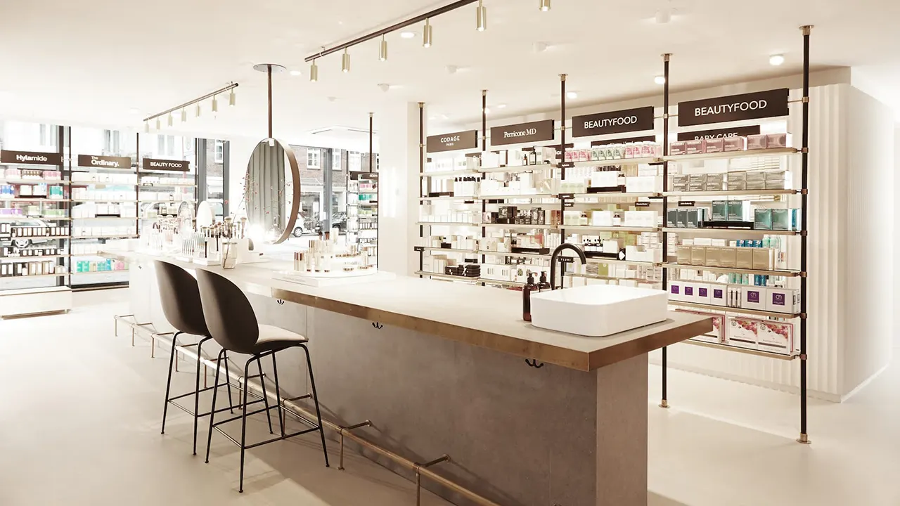 Modern, bright beauty store interior with shelves full of skincare and wellness products. A central table with stools and a sink is positioned under hanging lights, creating a clean and inviting atmosphere.