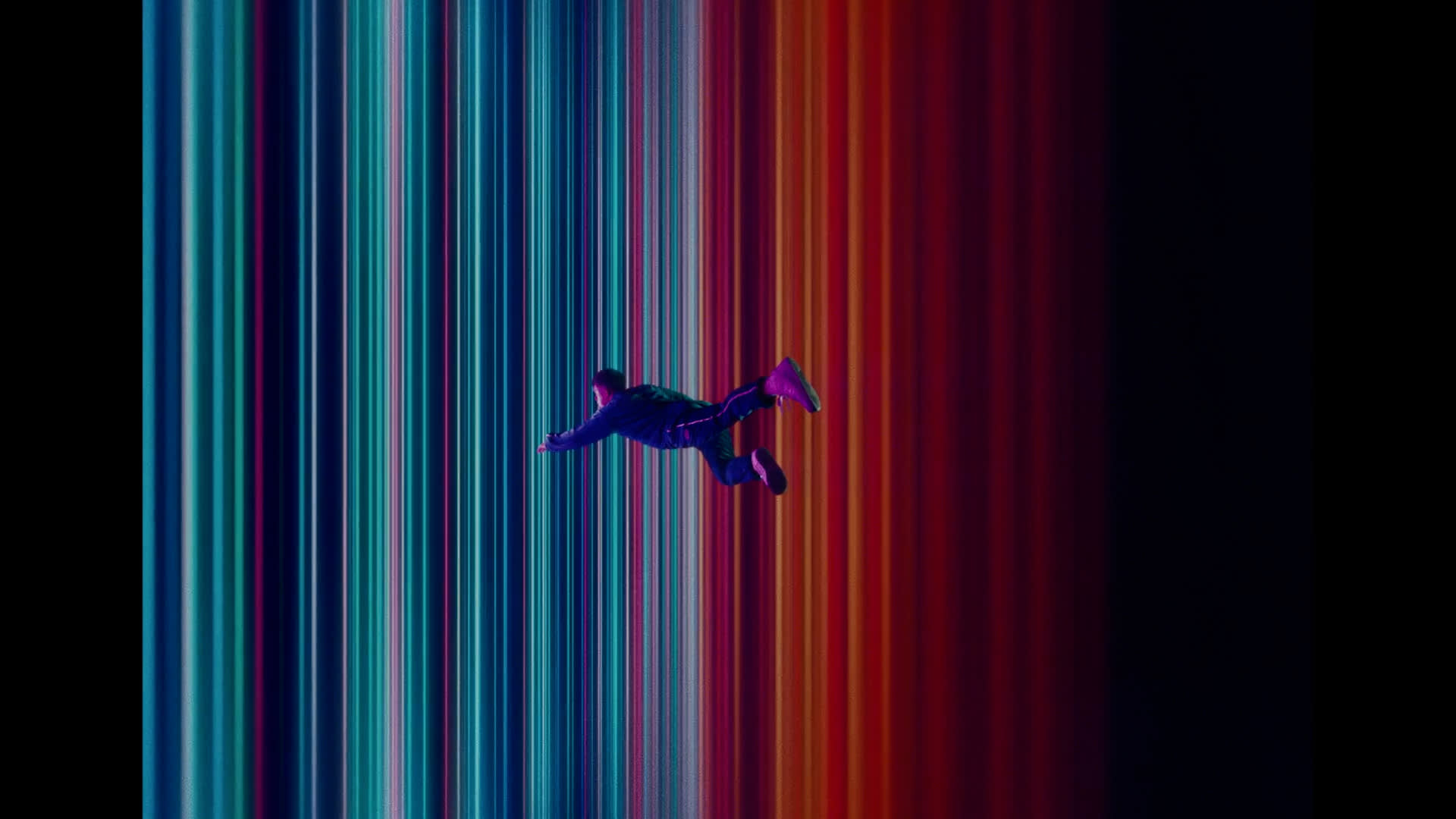 A person appears to be floating or falling in front of vibrant, vertical stripes of blue, teal, red, and orange light, creating a surreal, sci-fi atmosphere.