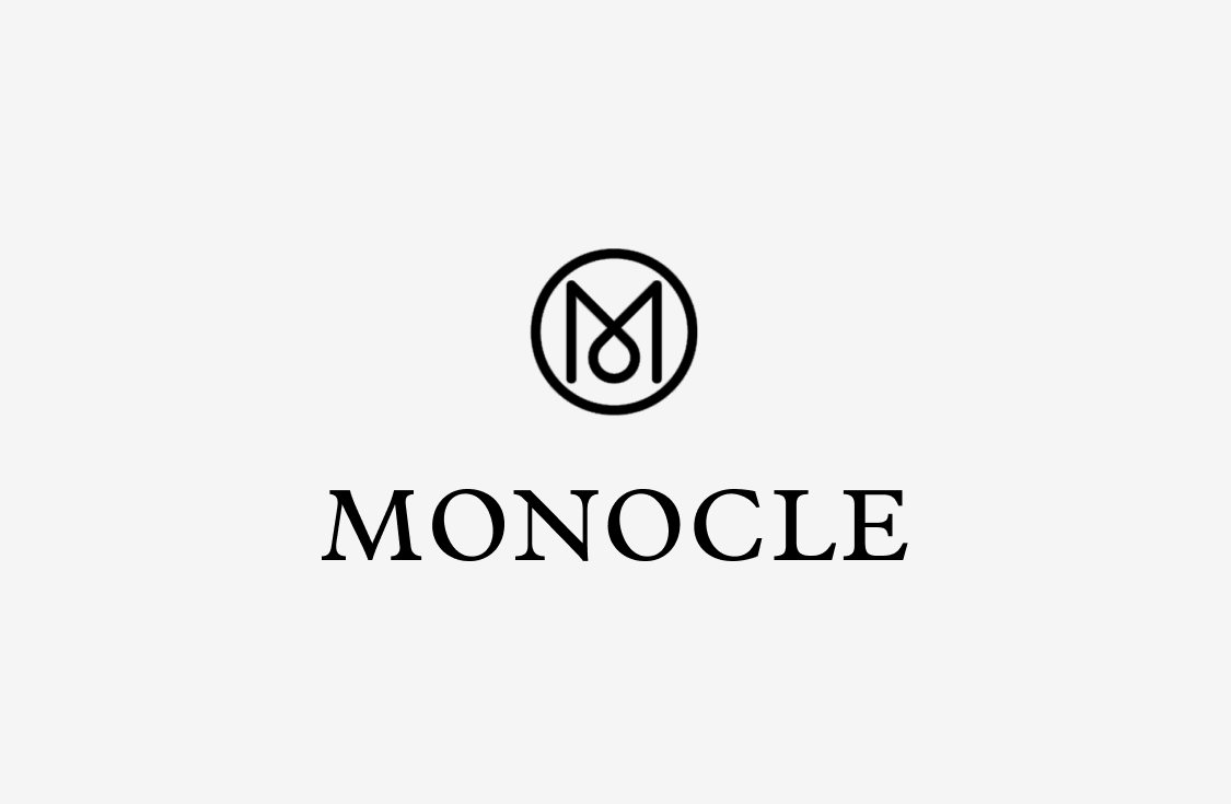 Monocle logo featuring a circular emblem with a stylized letter M above the word MONOCLE in bold, elegant black serif font on a white background.
