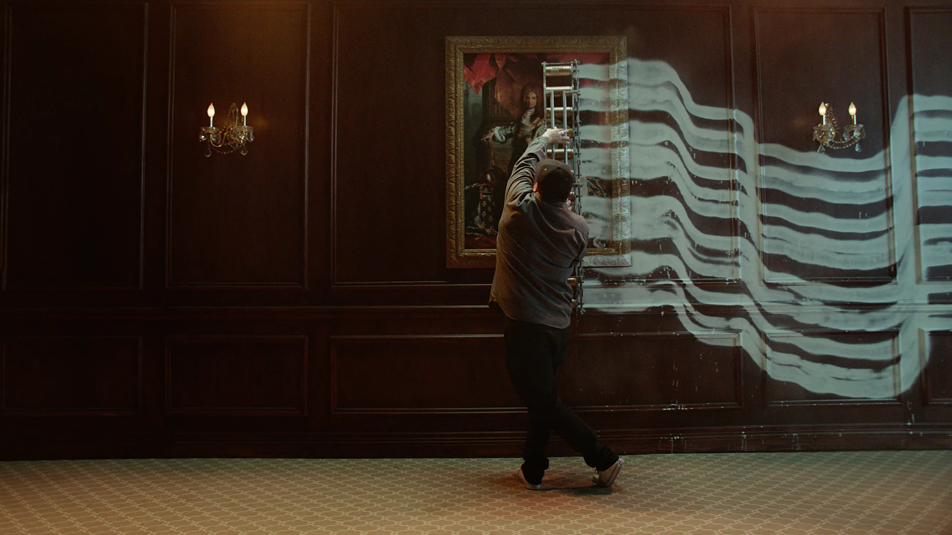 A person stands in front of a wood-paneled wall, painting thick white stripes across a framed portrait and the wall, with light from wall sconces illuminating the scene.