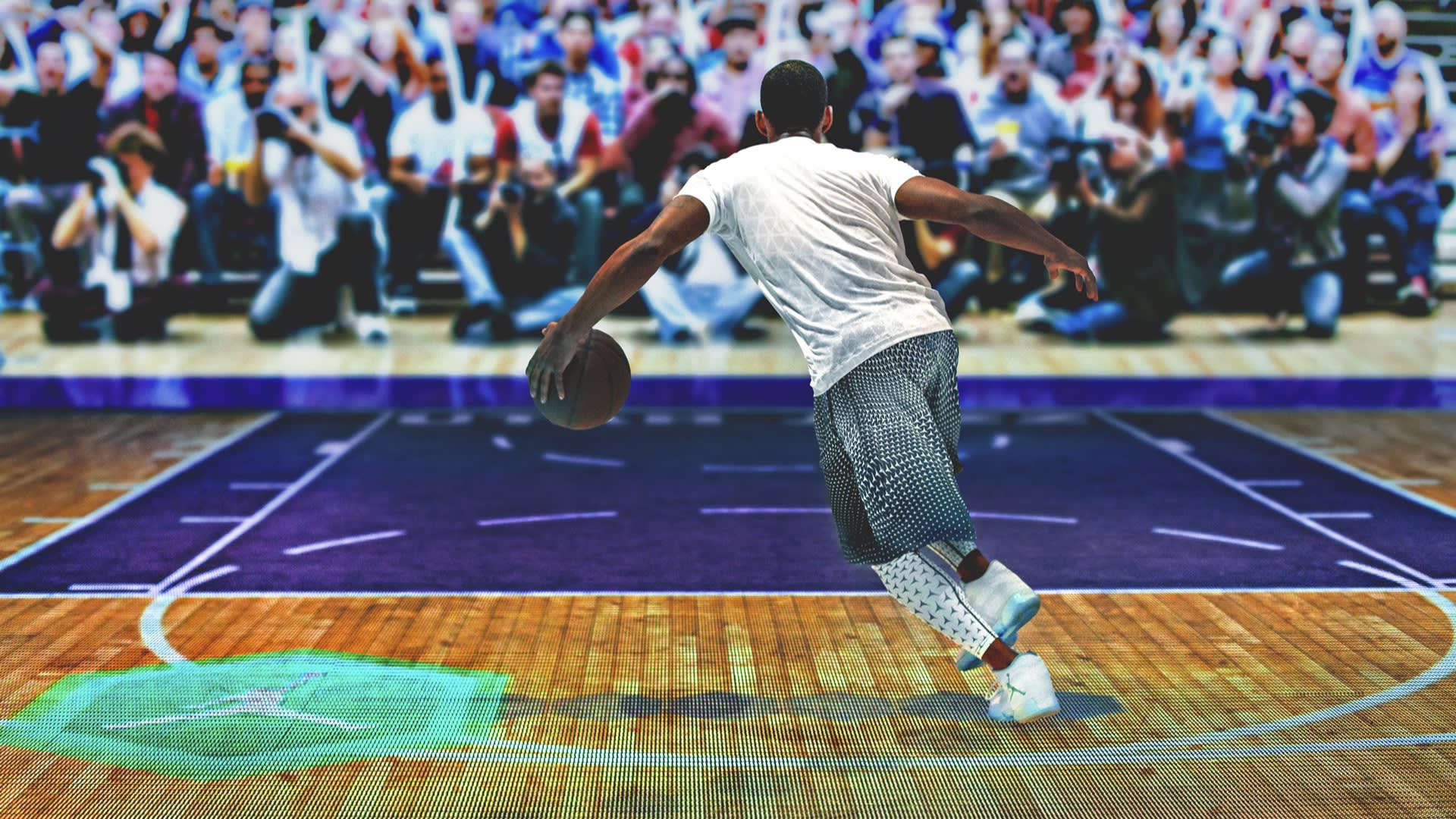A basketball player dribbles toward the hoop on a court, with a large, blurred crowd in the background. The scene is energetic, with the player in motion and the court brightly lit.