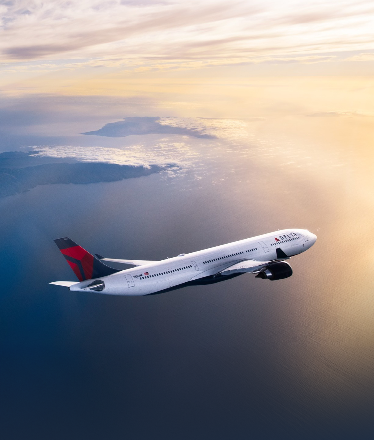 A Delta airplane flies above the ocean and amongst the clouds.
