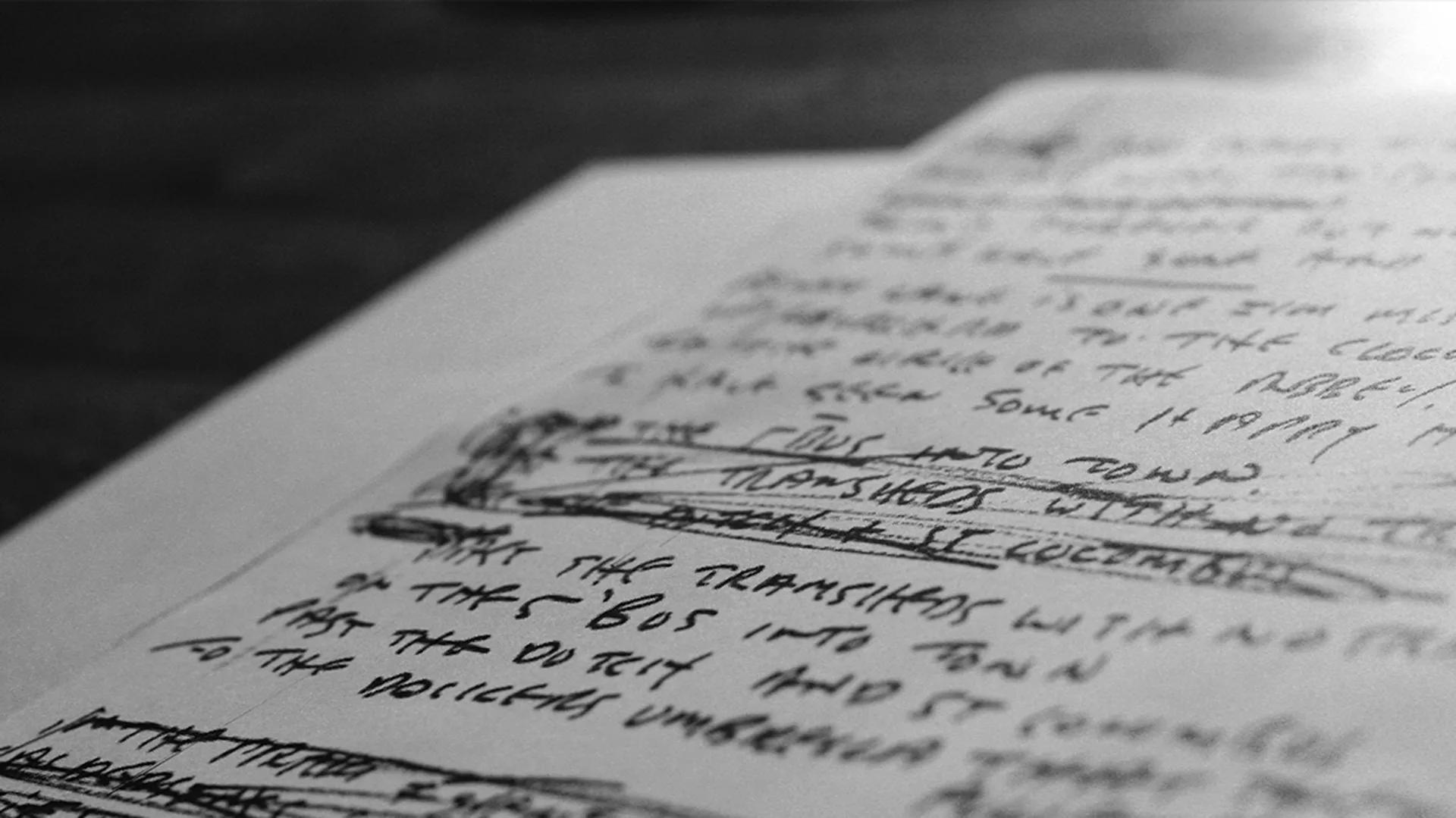 A close-up, black-and-white photo of handwritten, heavily scribbled notes on white paper, with text crossed out and blurred, giving an impression of brainstorming or draft writing.
