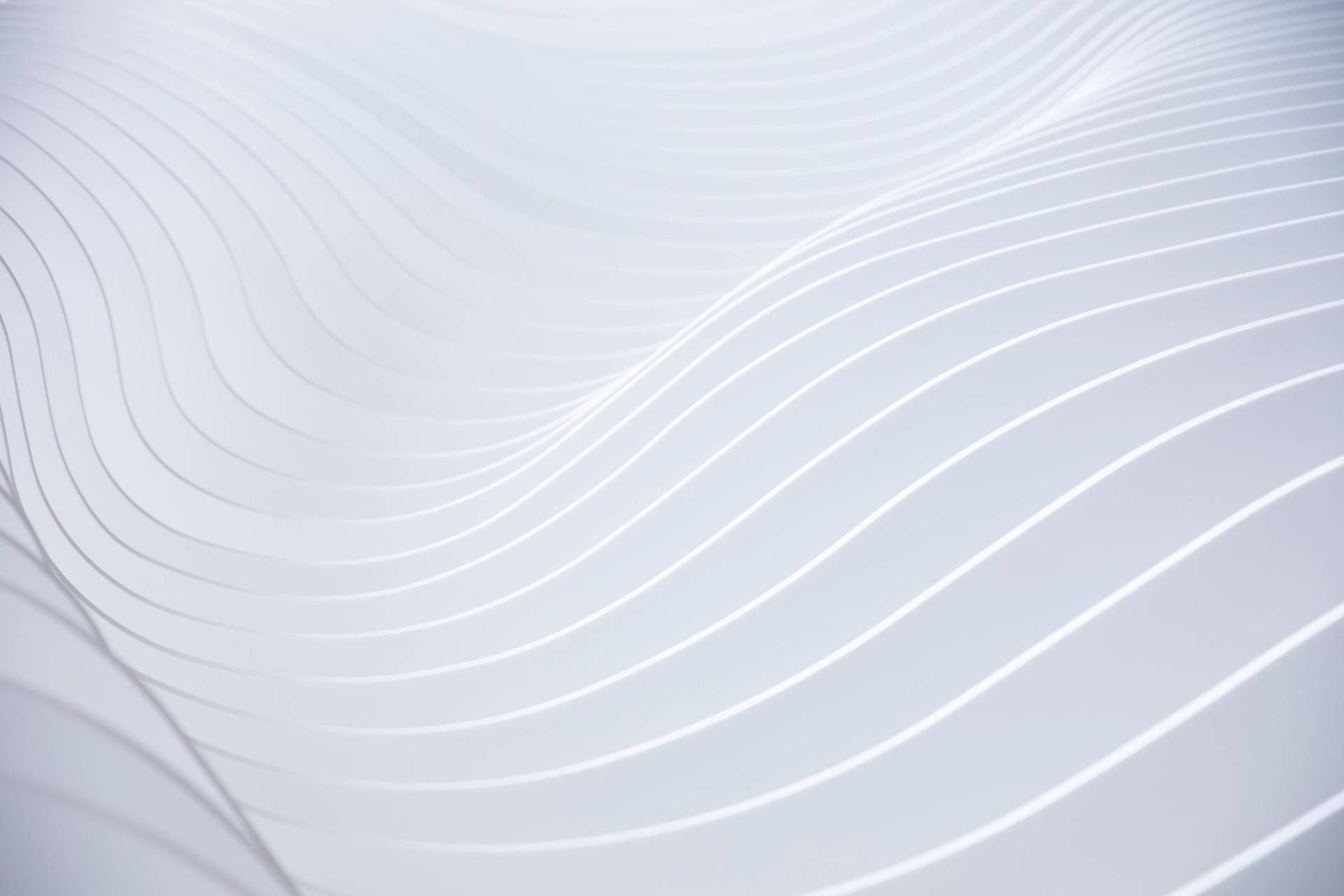 Abstract image of smooth, flowing white lines curving in parallel waves across a pale background, creating a sense of gentle movement and minimalistic, modern design.