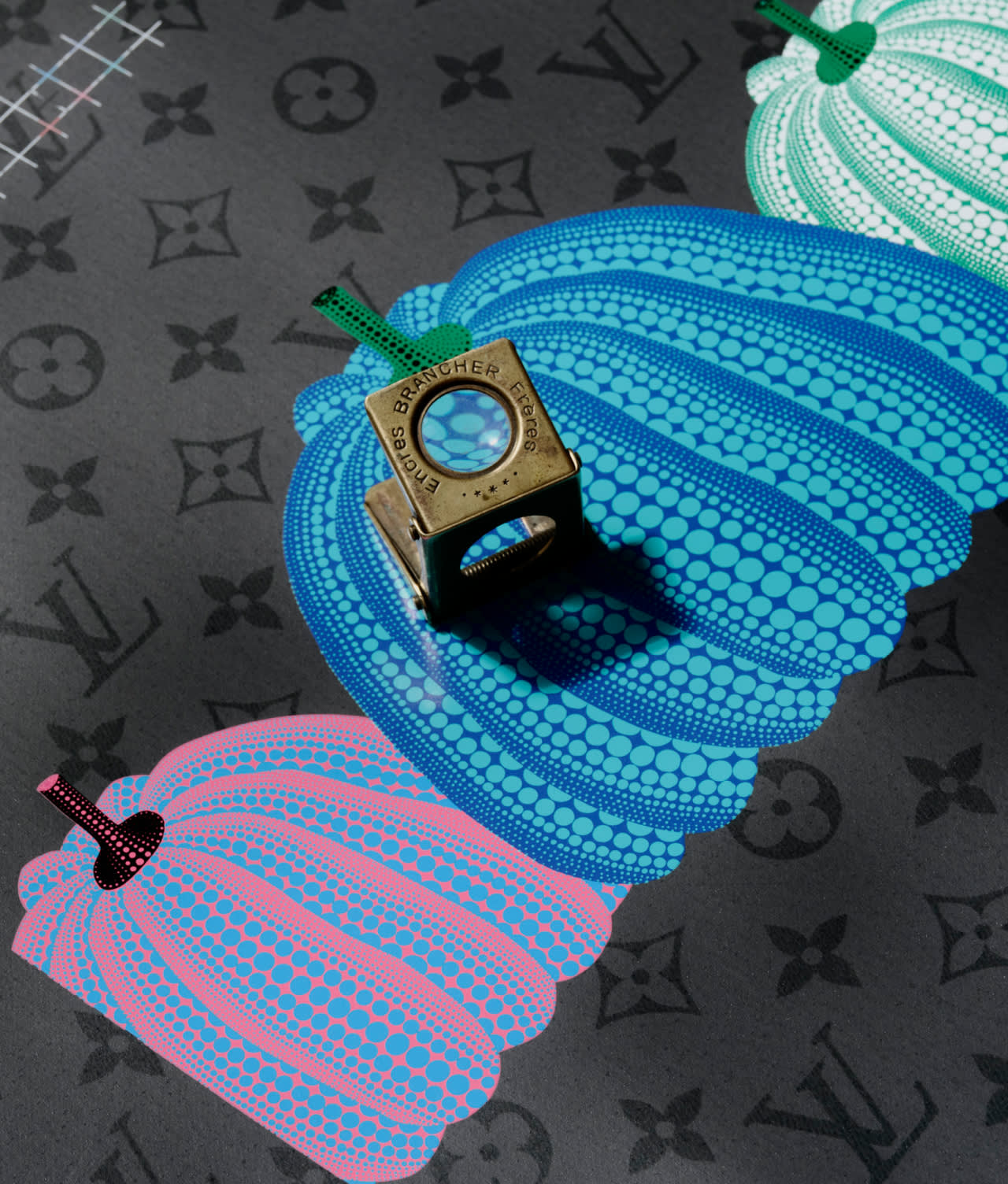 A brass Louis Vuitton cube rests on a patterned surface featuring stylized blue and pink pumpkins with dotted designs and green stems, overlaid on a gray Louis Vuitton monogram background.