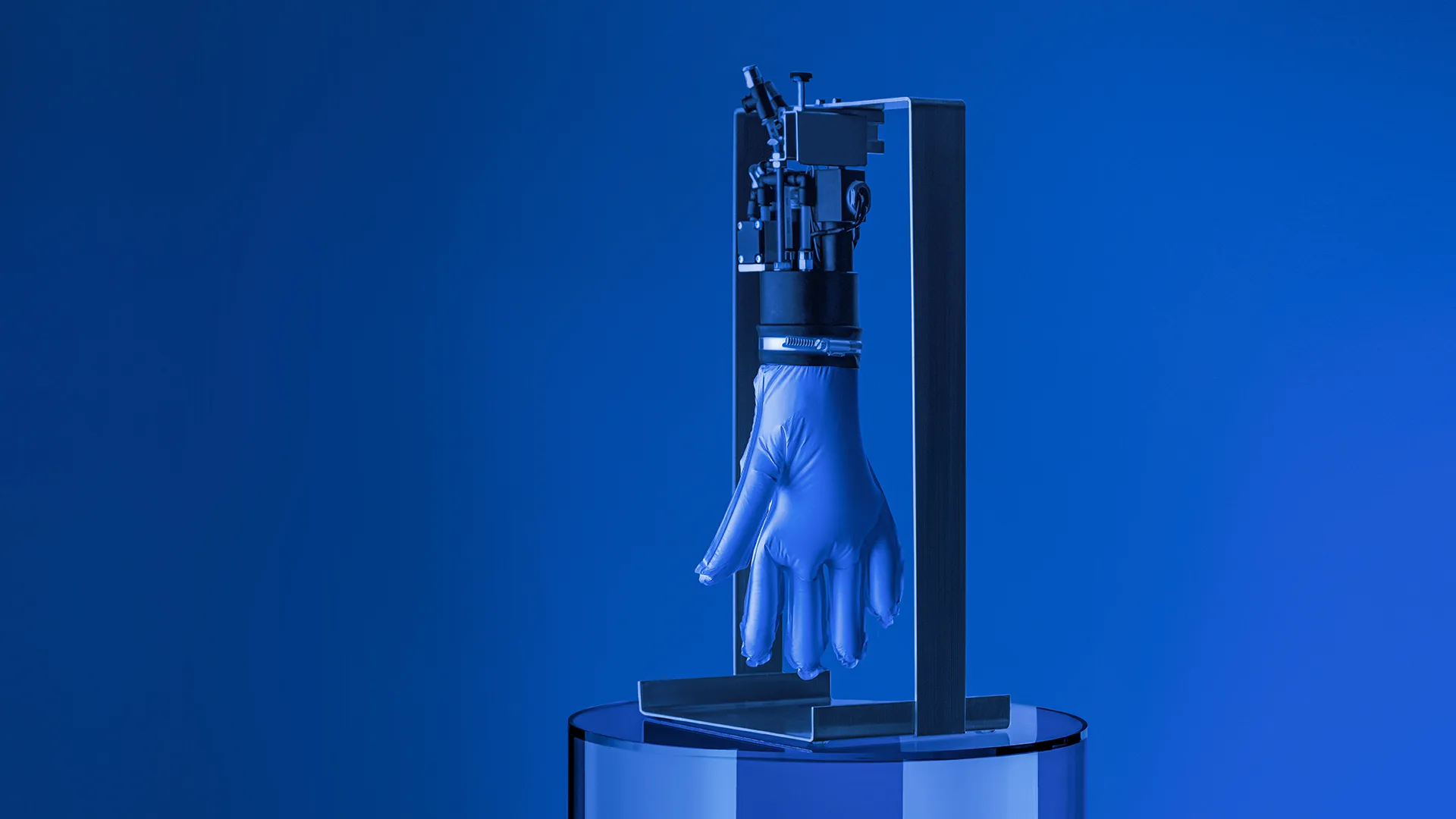 A robotic device holds an inflated blue latex glove upright, with the glove resembling a hand, against a blue background. The setup is positioned on a round, reflective surface.