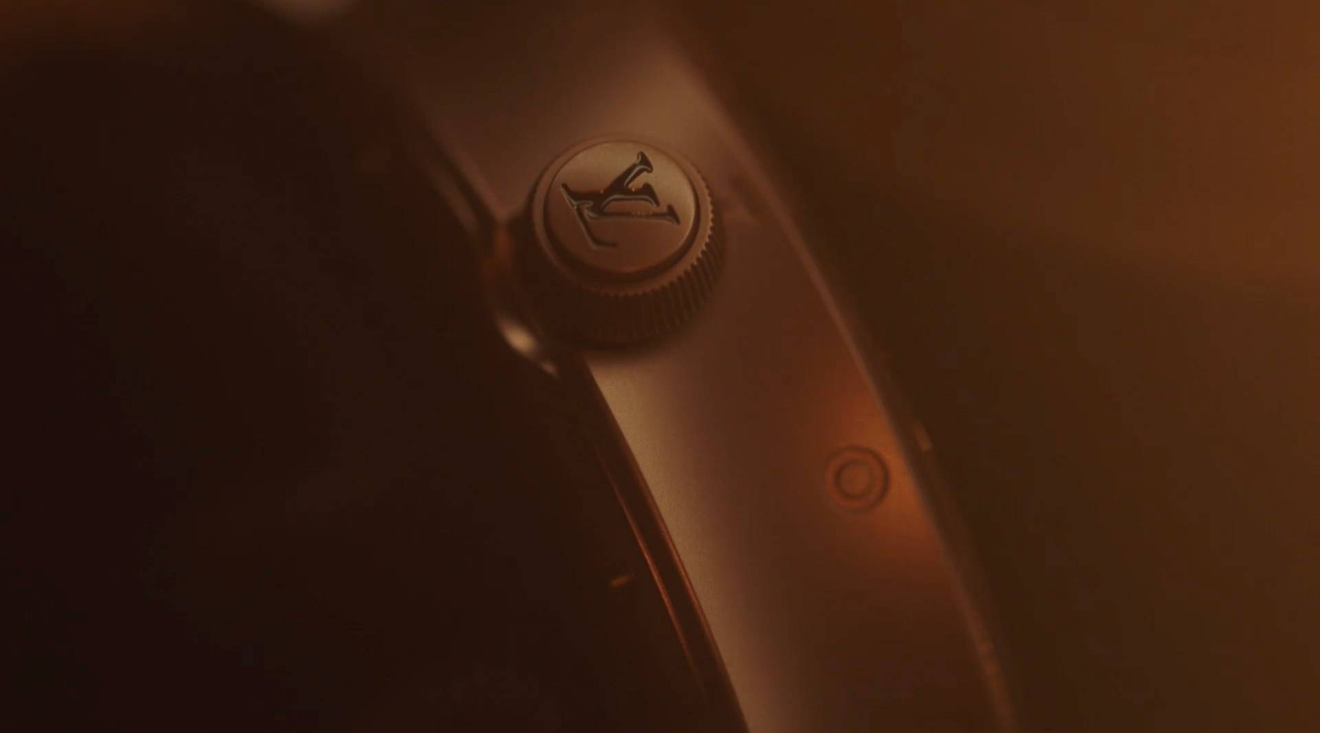 A close-up of a watch crown featuring an embossed logo of a prancing horse, with a warm, soft light creating a moody and luxurious atmosphere.