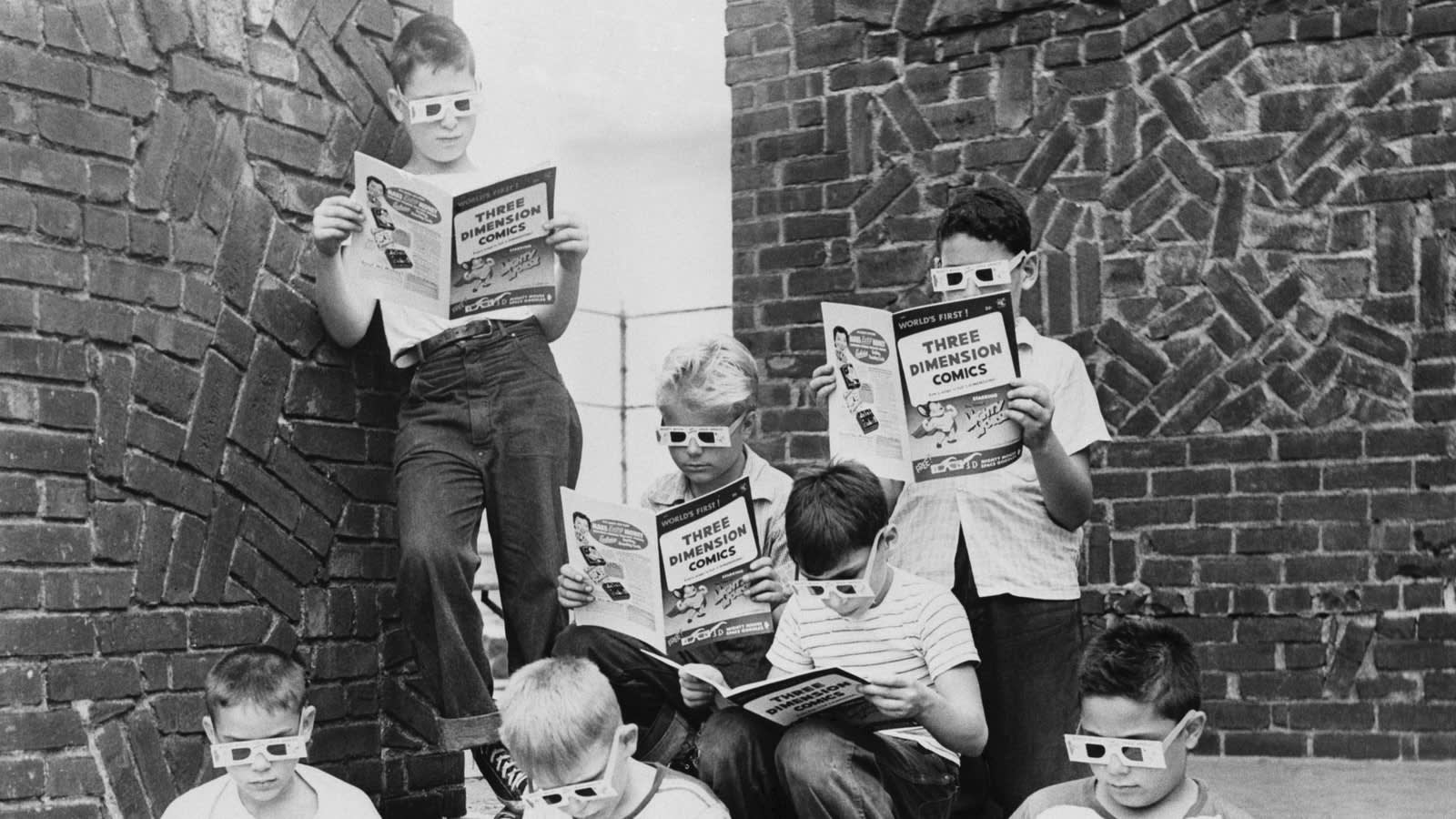 A group of boys wearing 3D glasses read Three Dimension Comics while sitting and standing against a brick wall outdoors.
