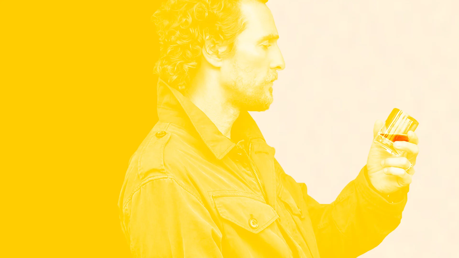 A man with curly hair wearing a jacket holds a glass of brown liquid, looking at it closely. The image has a strong yellow overlay on the left side, fading to a lighter tone on the right.