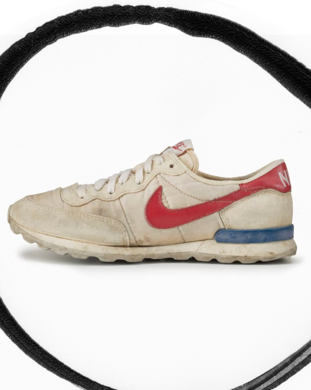 A worn, vintage white Nike running shoe with a red swoosh, red heel accent, blue midsole detail, and white laces is displayed inside a circular black border on a plain white background.