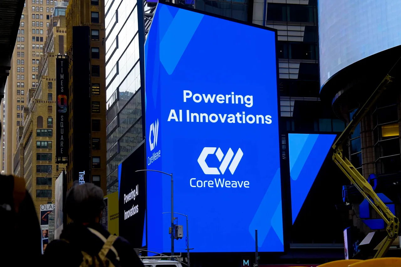 A large digital billboard in a city displays the text Powering AI Innovations and CoreWeave with the companys logo, surrounded by tall buildings and silhouettes of people in the foreground.