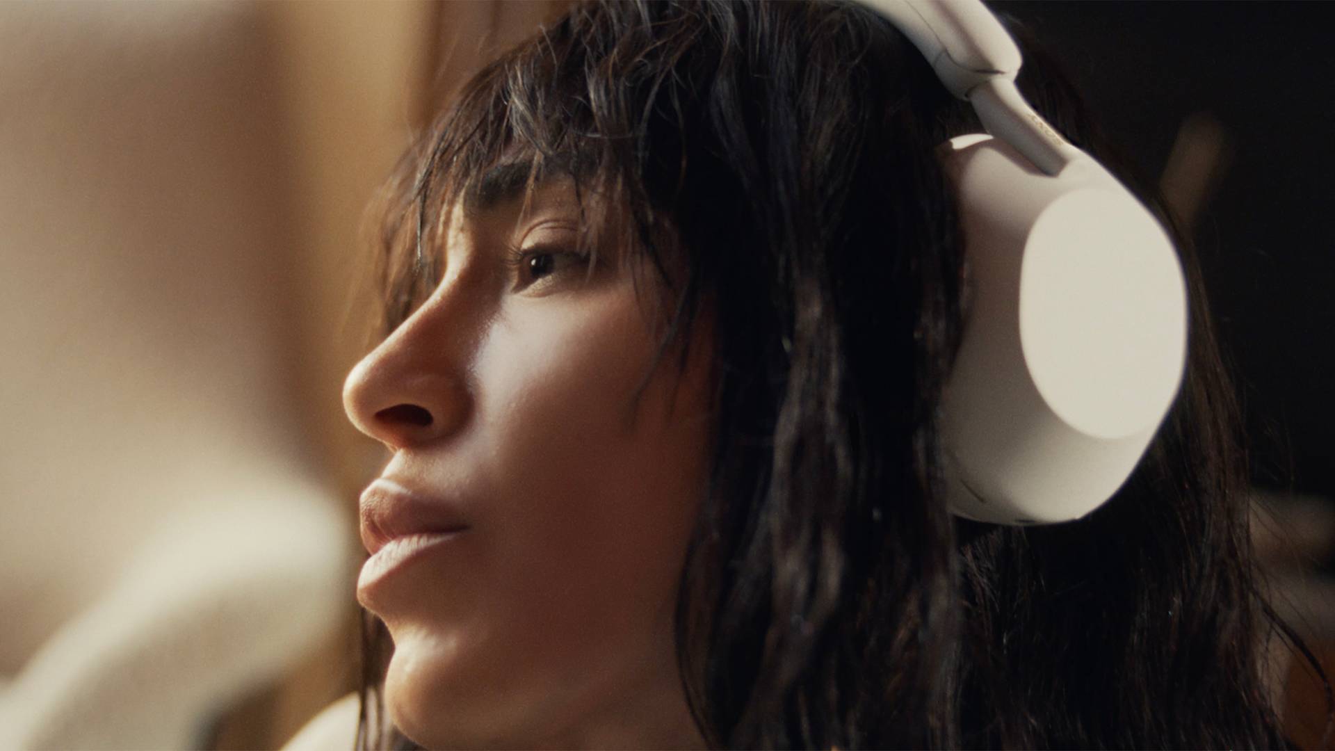 Close-up of Loreen with long dark hair wearing large white over-ear headphones, looking thoughtful and relaxed, with soft natural light highlighting their face.
