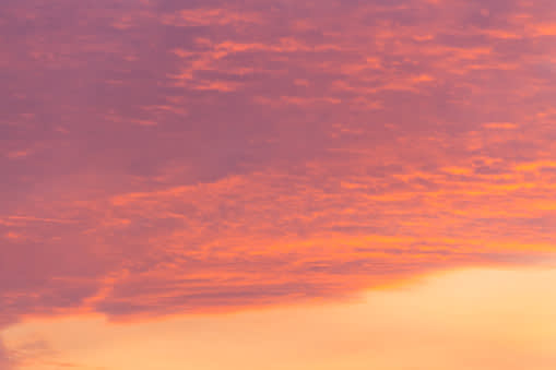 A vibrant sky filled with soft clouds in shades of pink, orange, and purple, illuminated by the warm light of sunrise or sunset.