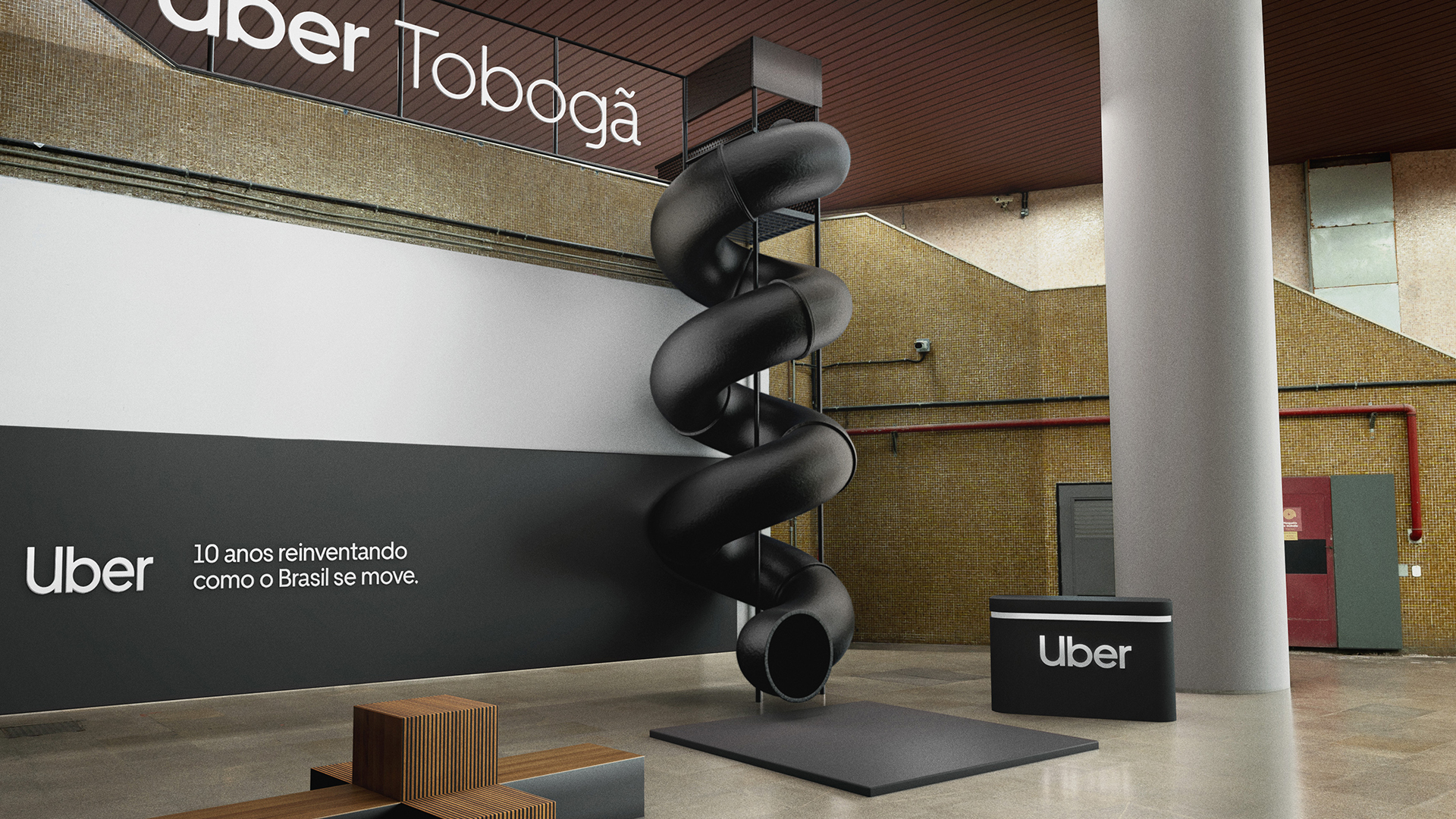 A large, spiral black slide labeled Uber Tobogã is installed indoors next to a wall with the text Uber: 10 anos reinventando como o Brasil se move. Modern seating and industrial decor are visible.
