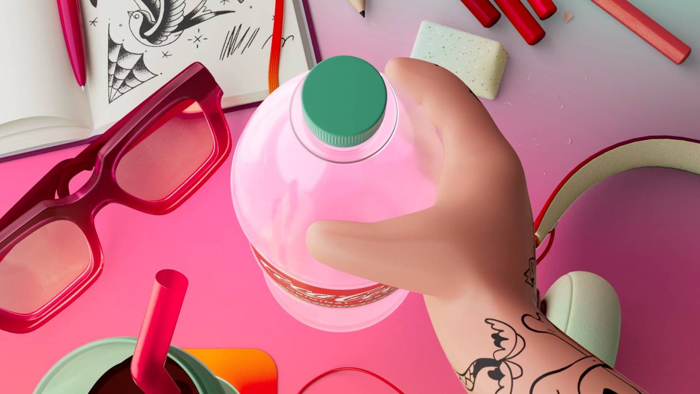 A hand with tattoos grabs a pink-capped bottle on a colorful desk with red glasses, an open sketchbook, pencils, an eraser, a cup with a straw, and other art supplies.
