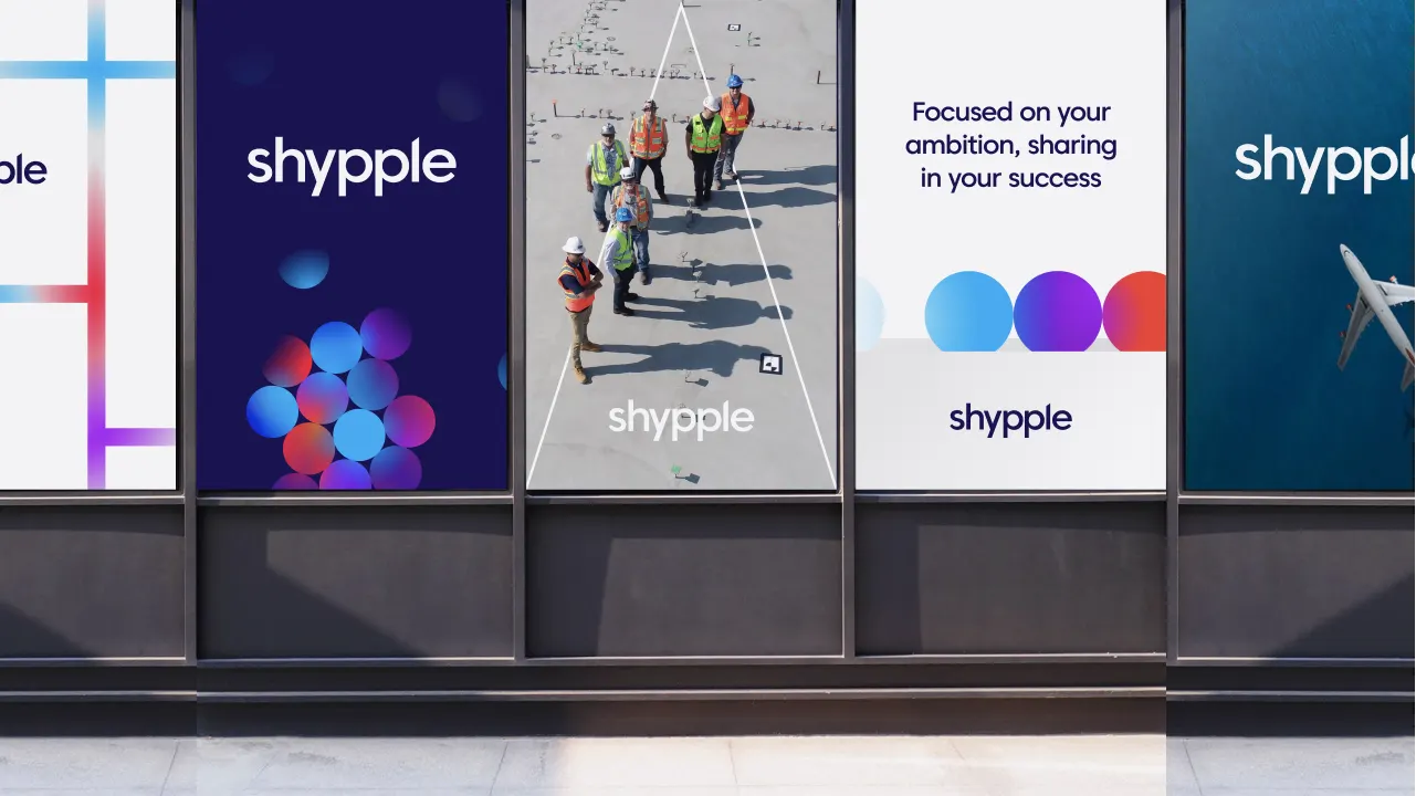 Five posters with the Shypple logo are displayed on a building, featuring colorful abstract designs, text about ambition and success, and one with construction workers and another with an airplane wing over water.
