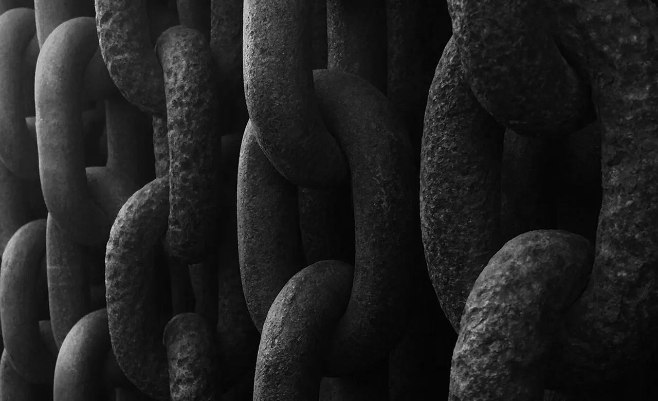 Close-up of several large, weathered metal chain links overlapping each other, creating a dark, textured, and industrial appearance.