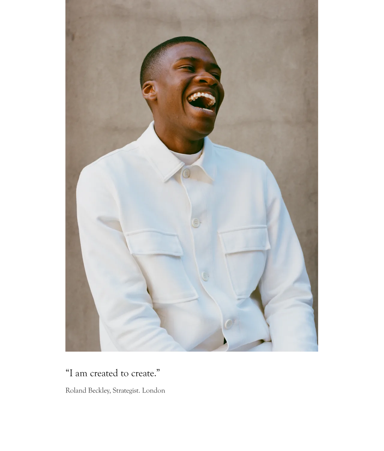A man wearing a white button-up jacket sits and laughs joyfully against a plain, light-colored background. The quote below reads, I am created to create.