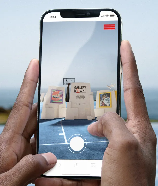 A person holds a smartphone, using an app to view virtual art displayed on a basketball court near the ocean. Three digital art pieces appear on the court through the phones screen.