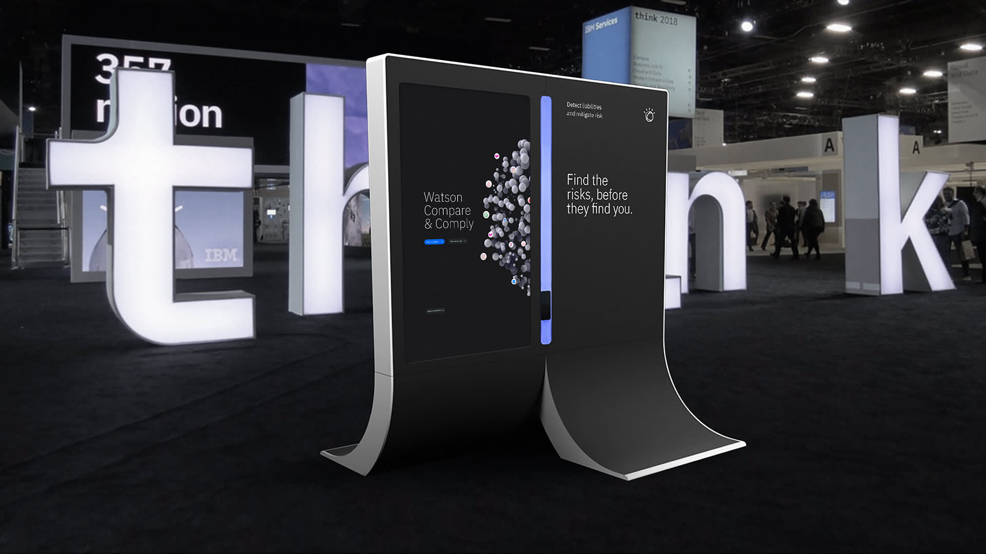 A sleek IBM digital display with curved edges stands on a black carpeted floor at an event, featuring Watson Compare & Comply and Find the risks, before they find you. Large illuminated think letters are in the background.