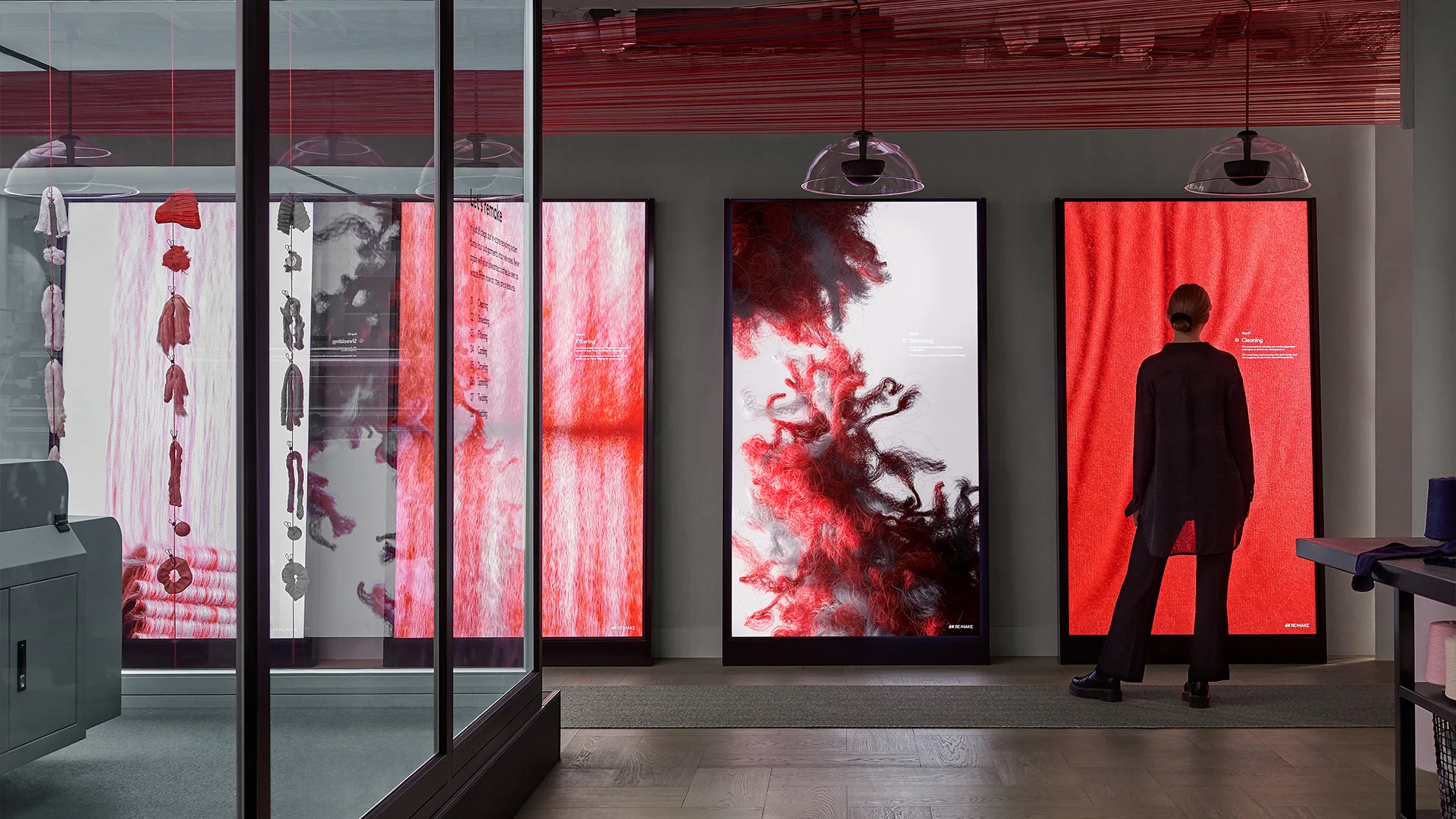 A person stands in front of three large digital screens displaying abstract red and white textile patterns in a modern, well-lit gallery or exhibition space.