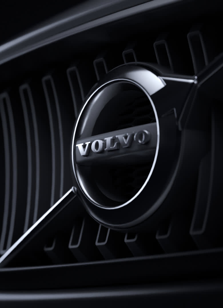 Close-up of a Volvo car grille featuring the chrome Volvo logo in the center, with vertical black grille slats in the background, all in dramatic lighting.