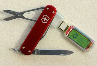 A red Swiss Army knife with extended scissors and blade, featuring a built-in USB flash drive on a light-colored surface.