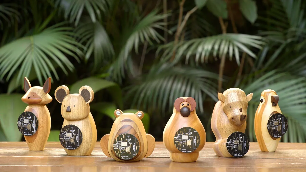 Five wooden animal figurines—fox, mouse, tiger, monkey, buffalo—stand on a wooden surface, each holding a black circuit board. Lush green plants fill the background.