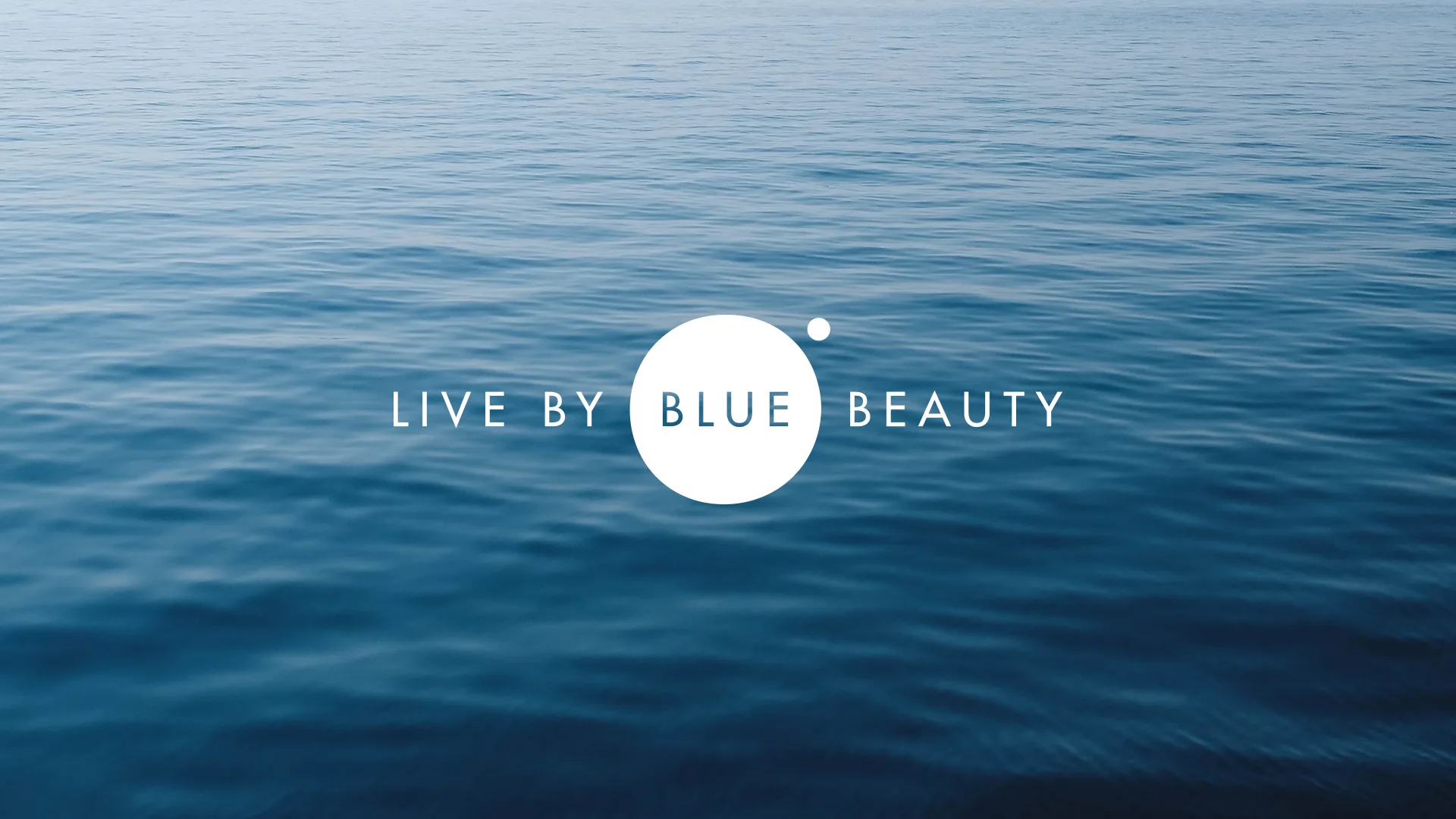 Calm blue ocean water with the words LIVE BY BLUE BEAUTY centered in white text, featuring a large white circle and a smaller dot over the word BLUE.