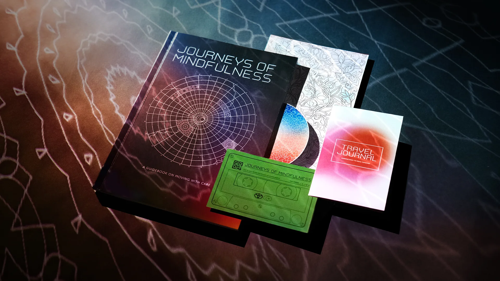 A book titled Journeys of Mindfulness lies on a patterned surface, accompanied by a green cassette tape, a travel journal, an illustrated booklet, and a CD. Soft, colorful lighting creates a calm, reflective mood.