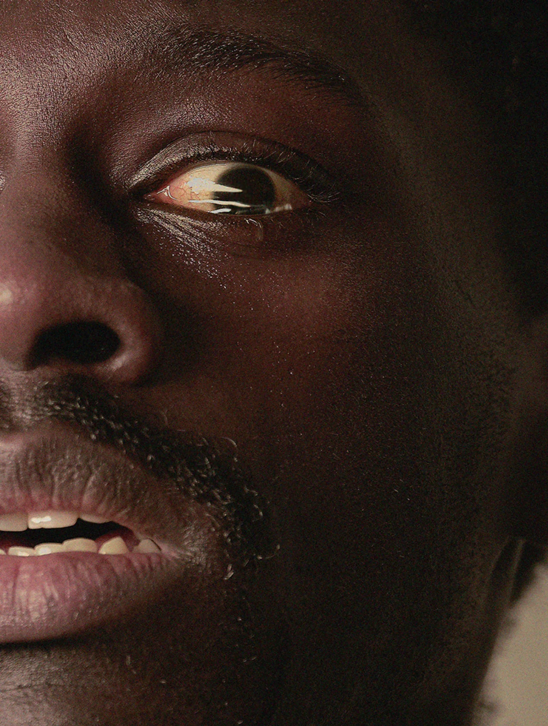 A close-up of a mans face showing a wide-open eye and slightly open mouth, conveying a strong expression of fear or shock.
