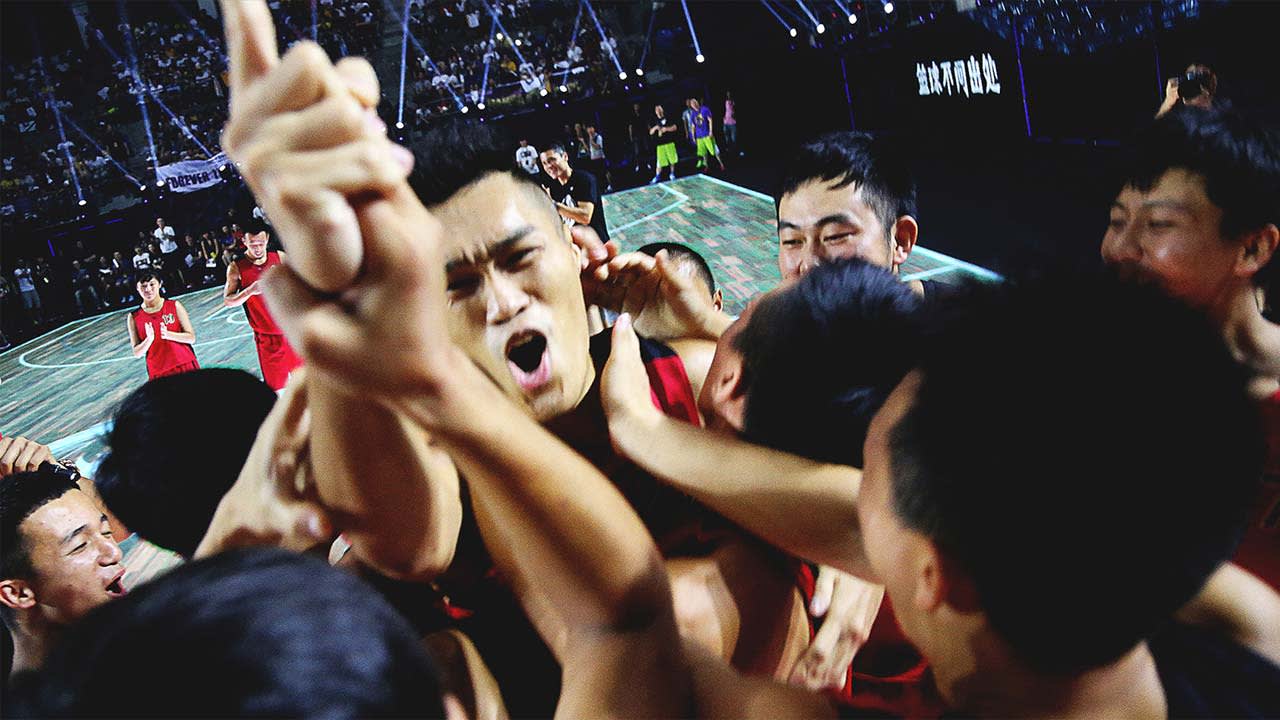 A group of basketball players in red jerseys celebrate excitedly on the court, cheering and hugging each other, surrounded by a lively crowd in a stadium.