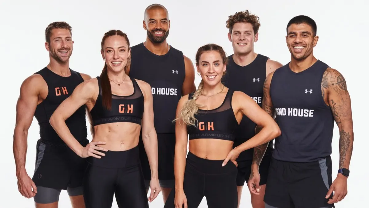 Six fit adults, three men and three women, stand in athletic gear smiling at the camera against a white background. Their tops display the words “GRND HOUSE.” They look confident, energetic, and ready to work out.