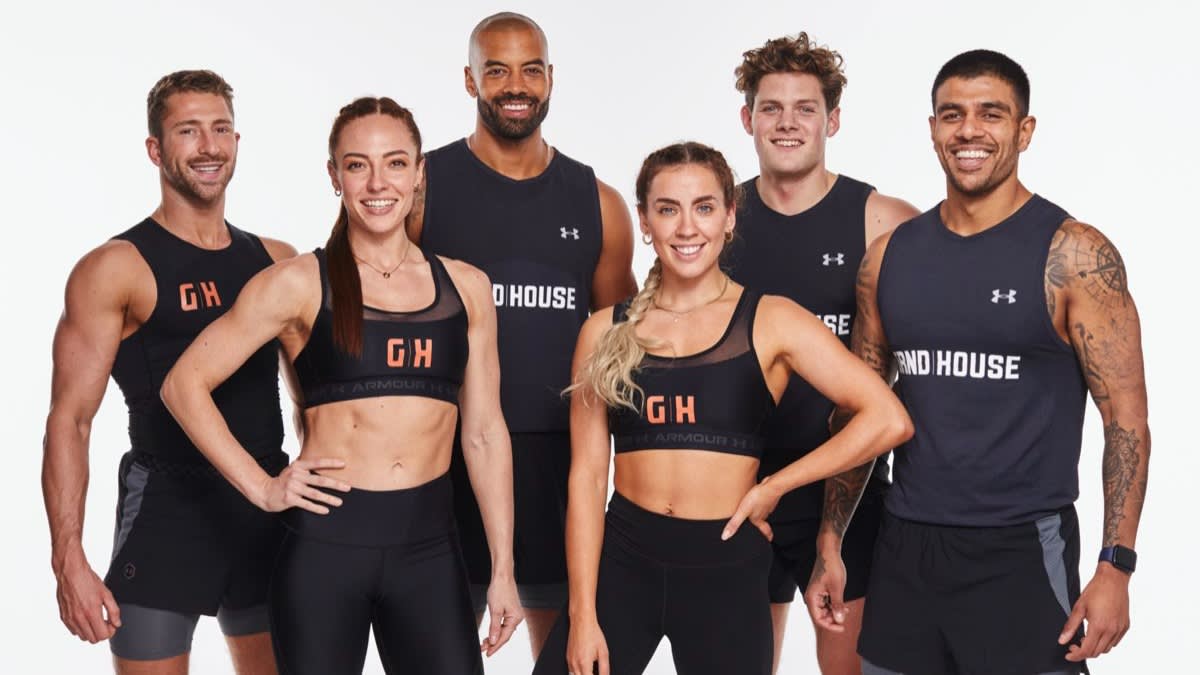 Six fit adults, three men and three women, stand in athletic gear smiling at the camera against a white background. Their tops display the words “GRND HOUSE.” They look confident, energetic, and ready to work out.