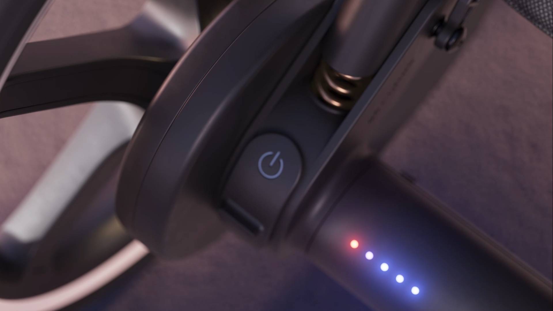 Close-up of a power button on an electric scooter handlebar, with four illuminated LED indicator lights showing battery level next to it and part of the wheel visible in the background.