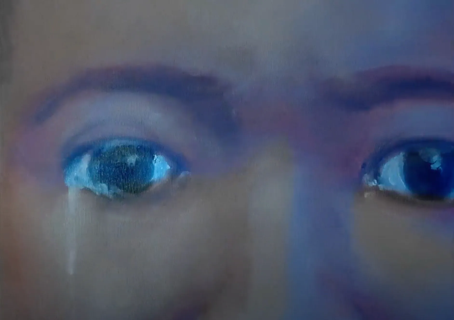 Close-up of a persons face showing both eyes with a blue tint across the image. The person appears to be looking intently forward, and there is a reflection of light in their eyes.