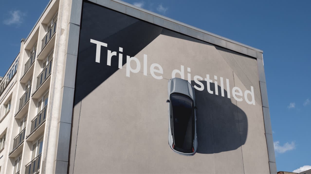 A car appears to be parked vertically on the side of a building, casting a shadow below. Large white text on the wall reads Triple distilled against a clear blue sky.