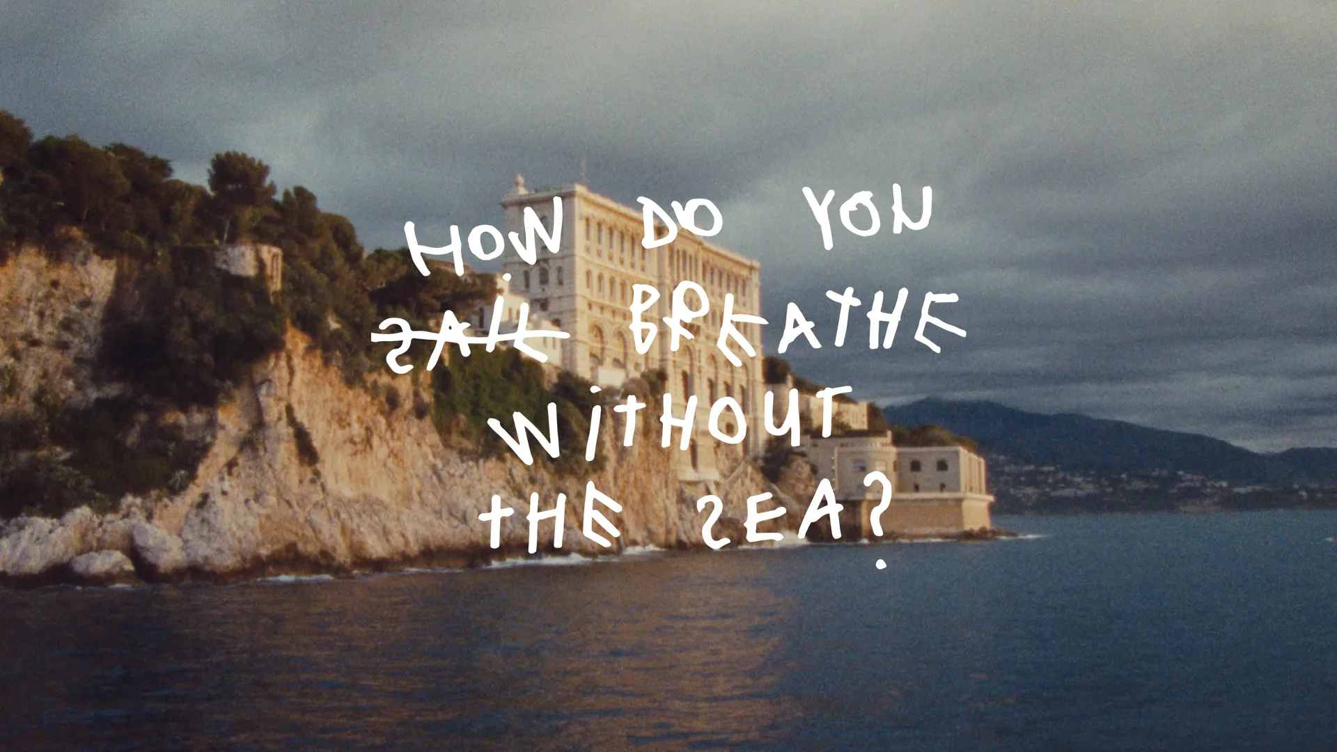 A stone building sits atop a rocky cliff by the sea, with handwritten text over the image reading, How do you all breathe without the sea?.