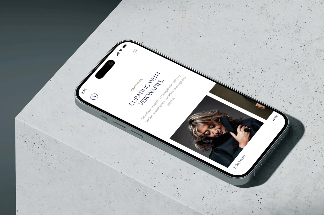 A smartphone rests on a light gray concrete surface, displaying a website article titled Curating With Visionaries with a photo of a woman making a creative hand gesture. The phone shows the time as 9:41 AM.