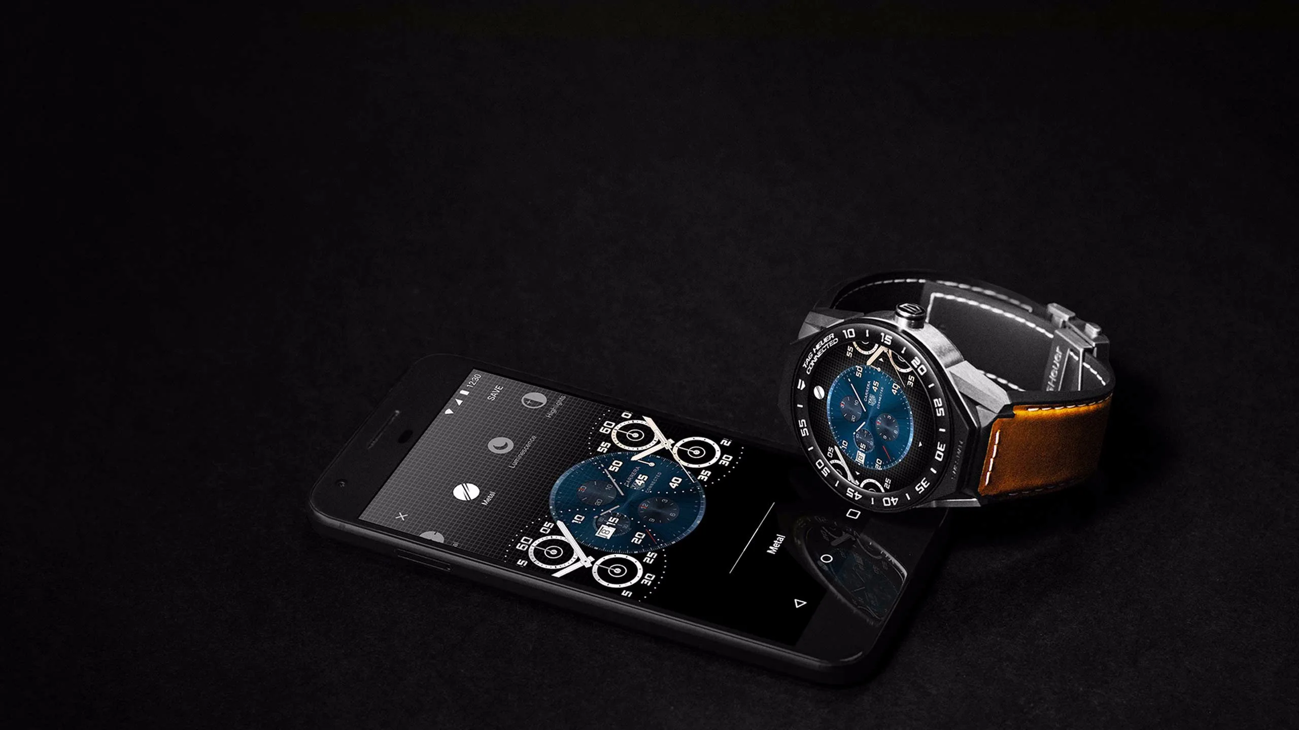 A smart wristwatch with a blue face and brown leather strap is placed on top of a black smartphone, which displays a matching watch face on its screen, all set against a dark background.