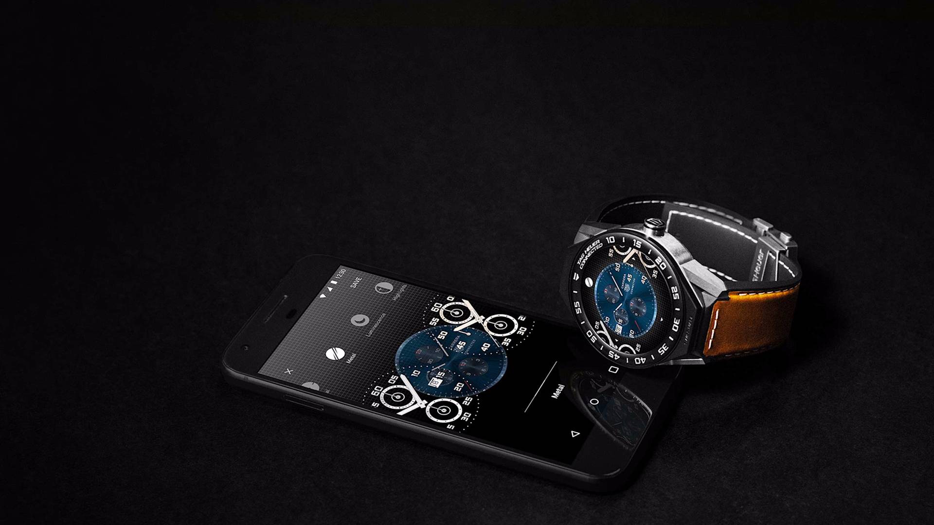 A smart wristwatch with a blue face and brown leather strap is placed on top of a black smartphone, which displays a matching watch face on its screen, all set against a dark background.