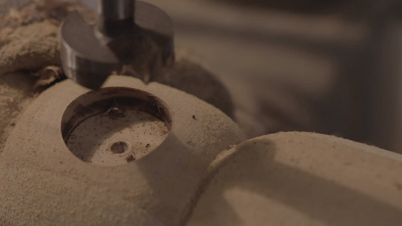 Close-up of a drill press making a circular hole in a piece of wood, with sawdust scattered around the work area.
