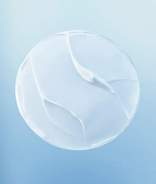 A close-up of a smooth, white, creamy substance spread in a circular shape against a soft blue background, showing subtle swirled texture.