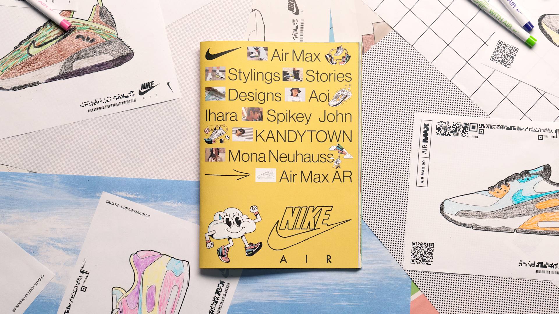 A yellow Nike Air Max booklet with playful illustrations and text is placed on a table surrounded by colorful sneaker sketches and design sheets. Pencils and printed designs are scattered around.