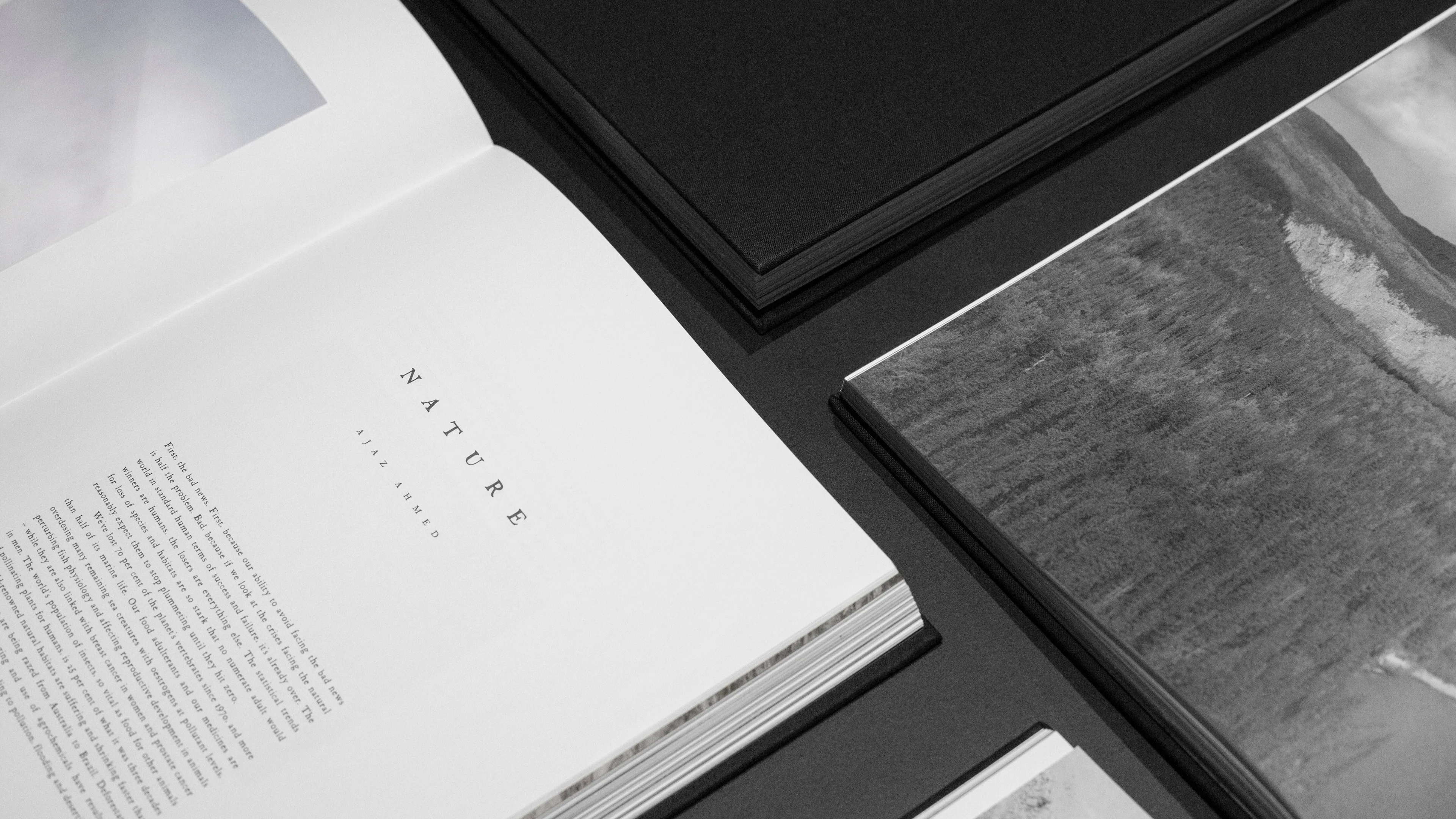 A close-up of open books and magazines on a dark surface, featuring black-and-white photography and a page with the heading NATURE in minimal, clean typography.