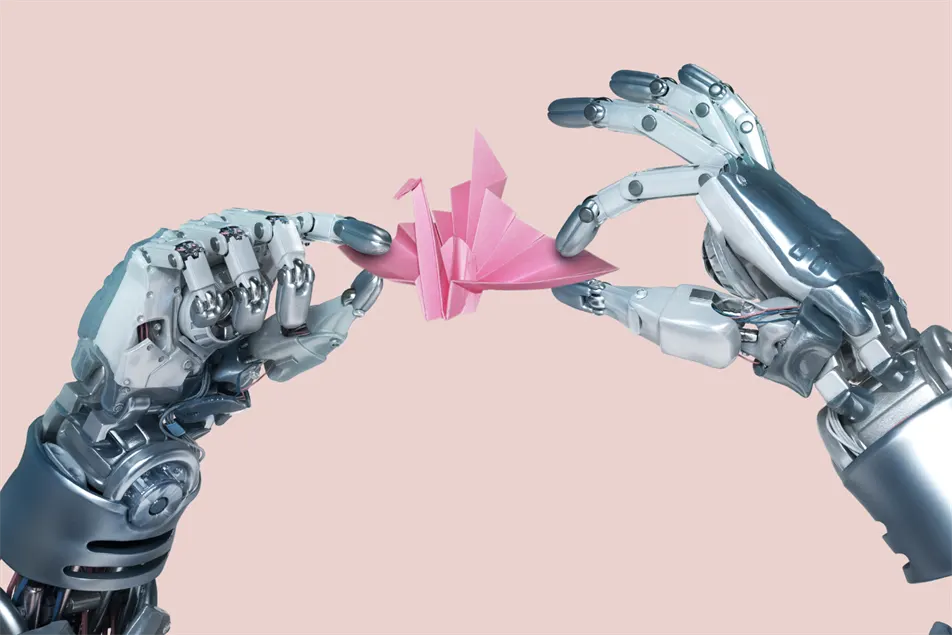 Two robotic hands delicately hold a pink origami crane between their fingers, set against a pale pink background.