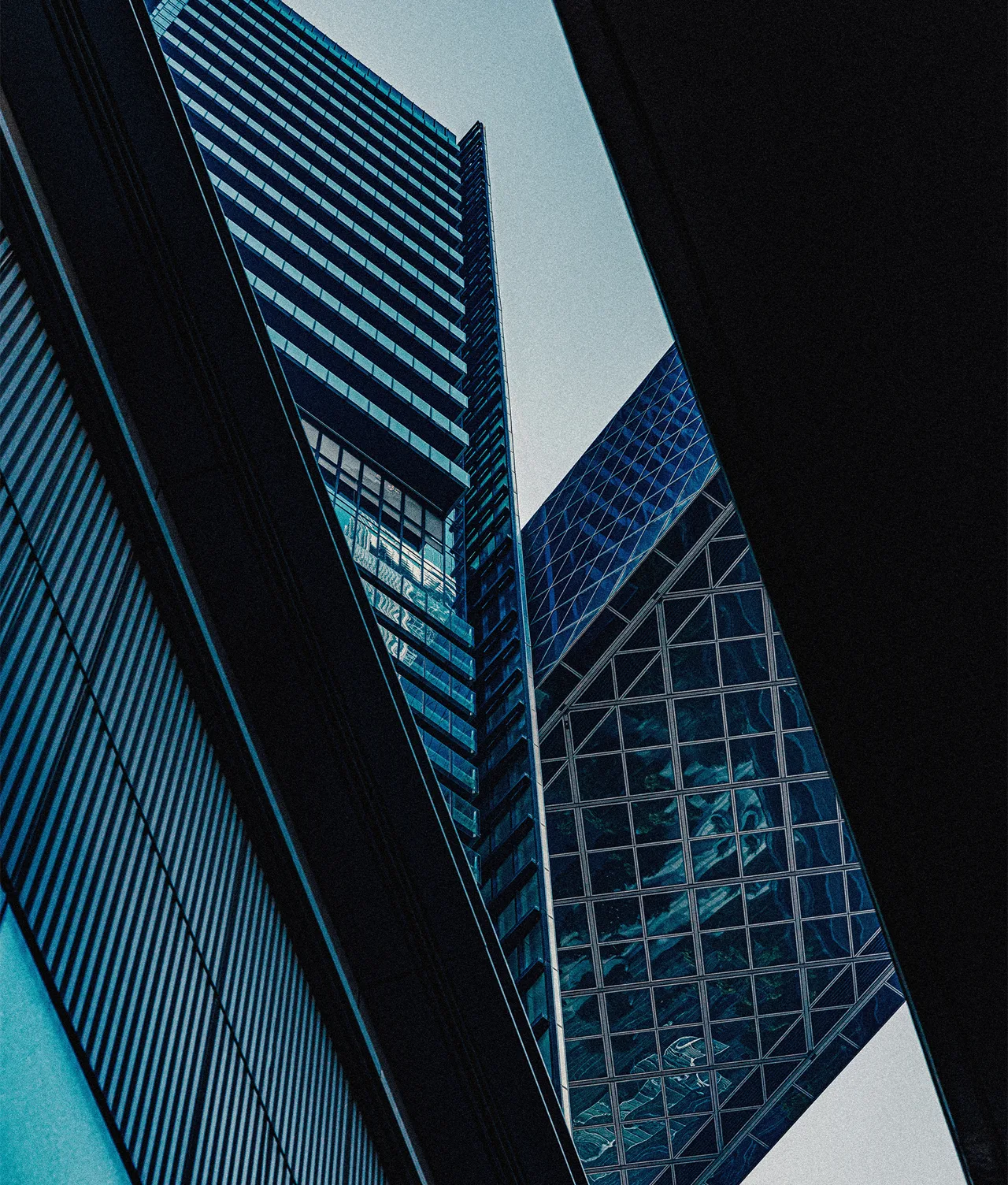 A dramatic, upward view of modern skyscrapers with glass and steel facades, intersected by dark architectural lines, against a cloudy sky. Geometric shapes and reflections dominate the urban scene.